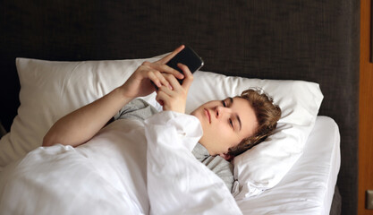 young man relaxing on her bed,using smartphone