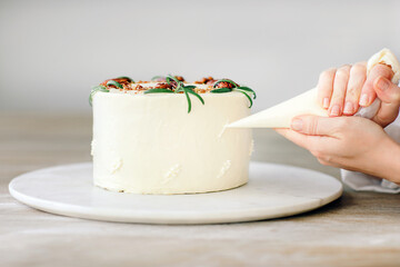 Confectioner  finishing  cake with pastry bag, close-up on hands. Wood and grey background.