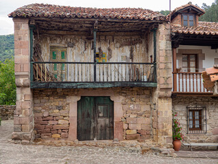 Fototapeta na wymiar Vista de una fachada antigua de piedra de una casa abandonada en ruinas, en el pueblo de Carmona, en la Cantabria rural de España, verano de 2020