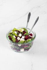 Appetizer. Beetroot, cottage cheese salad, diced, with arugula, black and white sesame seeds in a glass salad bowl on a white background