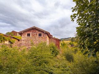 Vista de casas antiguas de piedra con cielo nuboso y hierbas verdes,  en el pueblo de Carmona, en la Cantabria rural de España, verano de 2020