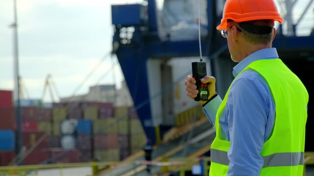 Cargo ship loading in dock. Professional worker with walkie-talkie reports to general manager about huge vessel loading in dockyard