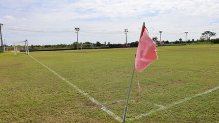 Obraz premium Old flagpole in the corner of the football field. Real dilapidated grass football field from use on white cloudy sky background with copy space. selective focus