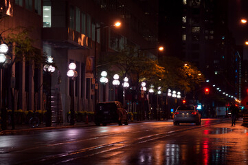 Rainy night view along a city street with a line of streetlamps, cars, light reflecting in wet asphalt surface