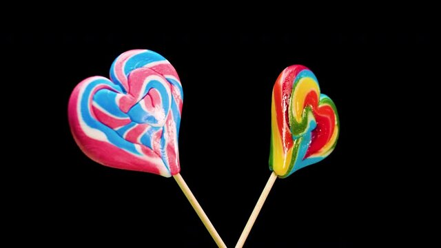 Mix of lollipops spiral spinning on a black background. Caramel candy on a stick in the shape of a heart.