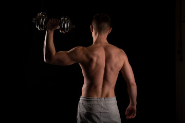 Fototapeta na wymiar Sport man Standing with Dumbbell in Hand. Man Working out with Dumbbell. Sportsman Back View