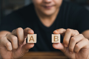 male hand holding a wooden cube with both hands letter A and B , business concept.