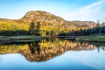 The Beehive, a rocky summit on Mt. Desert Island in Acadia National Park, Maine, is reflected upon Beehive Lagoon behind Sand Beach surrounded by trees with fall foliage color. - 470374358