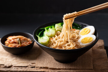 Korean spicy instant noodles soup with bok choy and boiled egg in a bowl eating with kimchi
