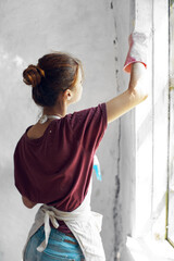Woman in a white apron paints a window in a house interior renovation