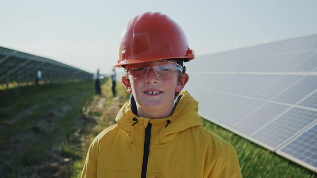 Portrait of cute young handsome kid wearing helmet smiling to camera in solar field. Solar farm construction. Alternative energy. Kids tour.