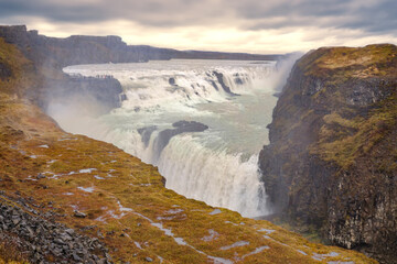 The Gullfoss waterfall in Iceland flows powerfully into a deep gorge below on an overcast mid-morning in October. 