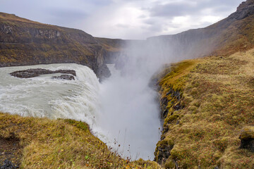 The Gullfoss waterfall in Iceland flows powerfully into a deep gorge below on an overcast mid-morning in October. 