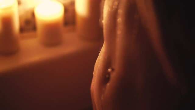 A young girl with freckles in a dark bathroom with candles washes her belly with a washcloth. Navel piercing