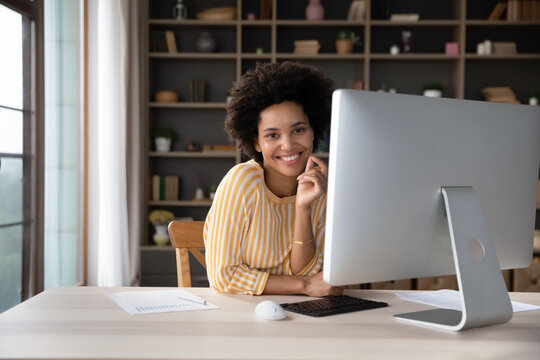 Happy Female African American Business Professional At Workplace Head Shot Portrait. Young Woman, Marketing Analyst, Employee Sitting At Big Workstation Monitor, Looking At Camera, Smiling