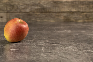 Ein Apfel links auf einer Platte vor einem hölzernen Hintergrund