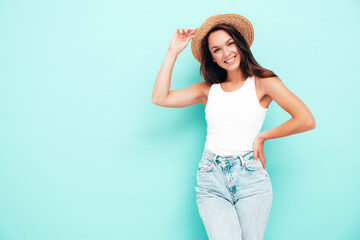 Young beautiful smiling female in trendy summer  clothes. Sexy carefree woman posing near blue wall in studio. Positive brunette model having fun. Cheerful and happy. In hat