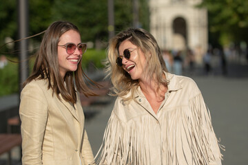 Fototapeta premium Two excited happy women walking together on the street. High Fashion amazed model woman posing in city street. Happy leisure, carefree weekend and romantic holiday.