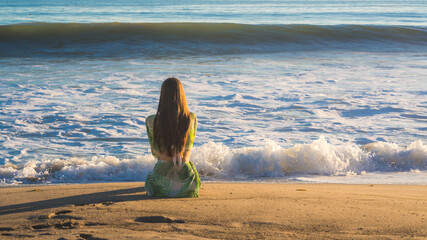Attractive young woman sitting on the beach looking at the ocean, Malibu, Los Angeles, California