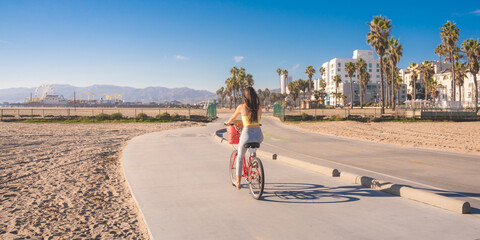 Attractive young woman riding bike near beach with palm trees, Santa Monica, Los Angeles, California - obrazy, fototapety, plakaty