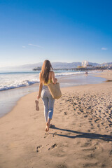 Fototapeta na wymiar Attractive young woman walking towards Santa Monica beach pier, Los Angeles, California