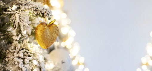 Decorated Christmas tree with a heart of gold. Banner. A branch of a snow-covered tree with Christmas decor with a soft focus. Copy space. Place for text
