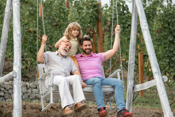 Excited grandfather father and son playing outdoors, sitting on the swing. Happy men family. Three men generation.