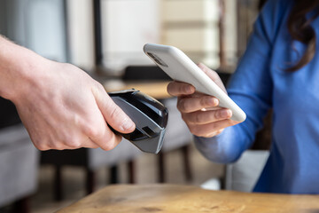 Paypass, male hands holding black pos terminal and female brings smartphone.
