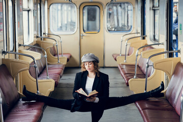 Flexible girl sitting on the split in retro underground carriage and reading book. Concept of...