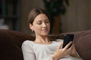 Calm attractive woman sit on sofa using smartphone, close up. Generation and modern tech everyday usage for fun, making distant order, communication remotely, web surfing, internet connection concept