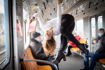  Gymnastic girl hanging upside down on the bar in subway and reading book. Concept of creativity,...