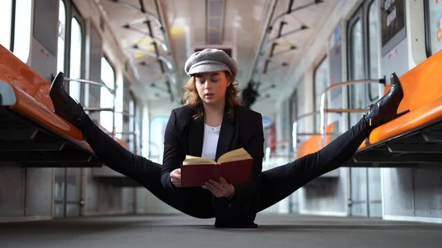 Flexible woman sitting on the split in the subway and reading book in slow motion. Concept of education and self-development 