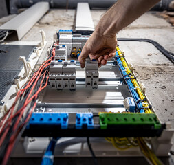 A male electrician works in a switchboard with an electrical connecting cable.