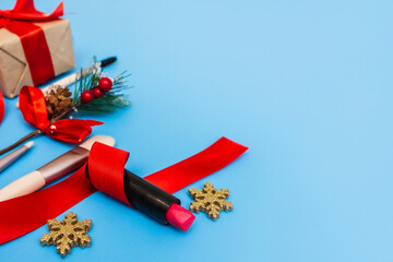Cosmetics, brushes, a Christmas gift, a red ribbon and gold stars are laid out on a blue background. Preparing for the party. Top view