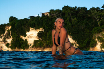 Obraz premium Portrait of surfer girl with beautiful body on surfboard in the ocean at colourful sunset time