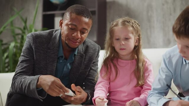 Concentrated black English tutor shows cards with letters teaching little children foreign language during home lesson with native speaker slow motion