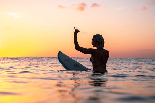 Portrait of surfer girl with beautiful body on surfboard in the ocean at colourful sunset time