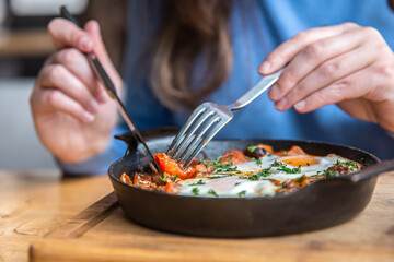 Close-up, a woman in a cafe dines on traditional shakshuka.