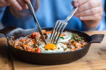 Close-up, a woman in a cafe dines on traditional shakshuka.