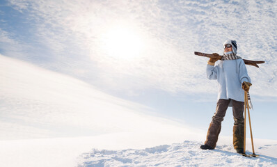 Boy on the old skis at the top of the hill. Young athlete and a happy winner in skiing stands on a snow-covered mountain against the background of the sky.