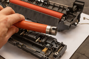 a view of a worn out upper heating shaft, roller from a printer in the hand of a person, a service center foreman who disassembles and repairs a thermoblock, a fuser from a printing office device