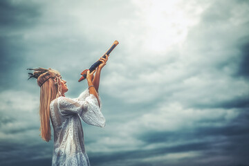 beautiful shamanic girl playing on shaman flute in the nature.