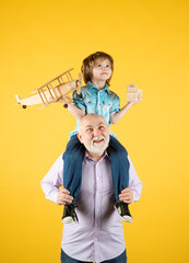 Grandfather and son piggyback ride with plane and wooden toy truck. Men generation granddad and grandchild. Elderly old relative with child.
