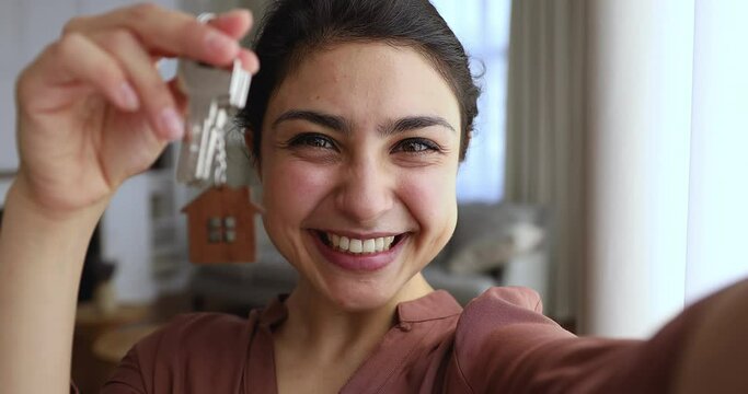 Overjoyed young woman hold keys shoot self video portrait on phone share great news of winning apartment in lottery at social network. Excited Indian lady own flat buyer make videocall demonstrate key
