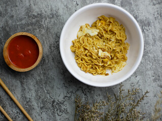 Fried noodles in a white bowl, with sauce in a small bamboo bowl
