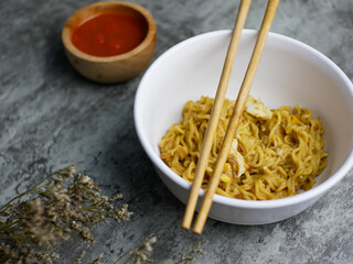 Fried noodles in a white bowl, with sauce in a small bamboo bowl