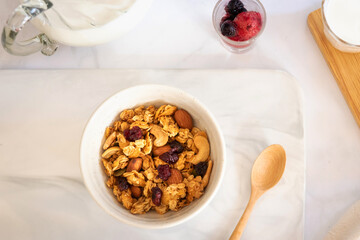 Granola with milk and berries in a white bowl; top view on white table. Healthy breakfast concept.