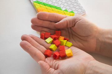 He holds a lot of colorful plastic parts of the designer in his hands. Rainbow elements in the hands. Choosing a future profession for a child. Methods of early child development