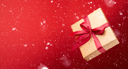 Christmas. A gift box with a red bow is flying or levitating in the air on a red background. Snow.