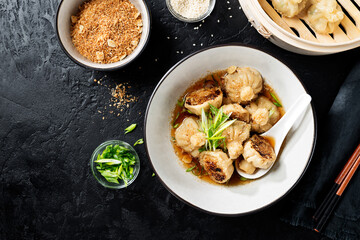 Sesame Chicken Dumplings in Spicy Broth with Garlic Crisps. Black background. top view